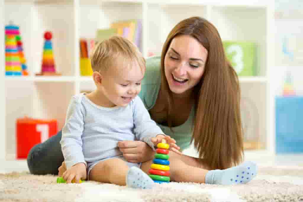 Nanny and toddler playing with toy activities on floor